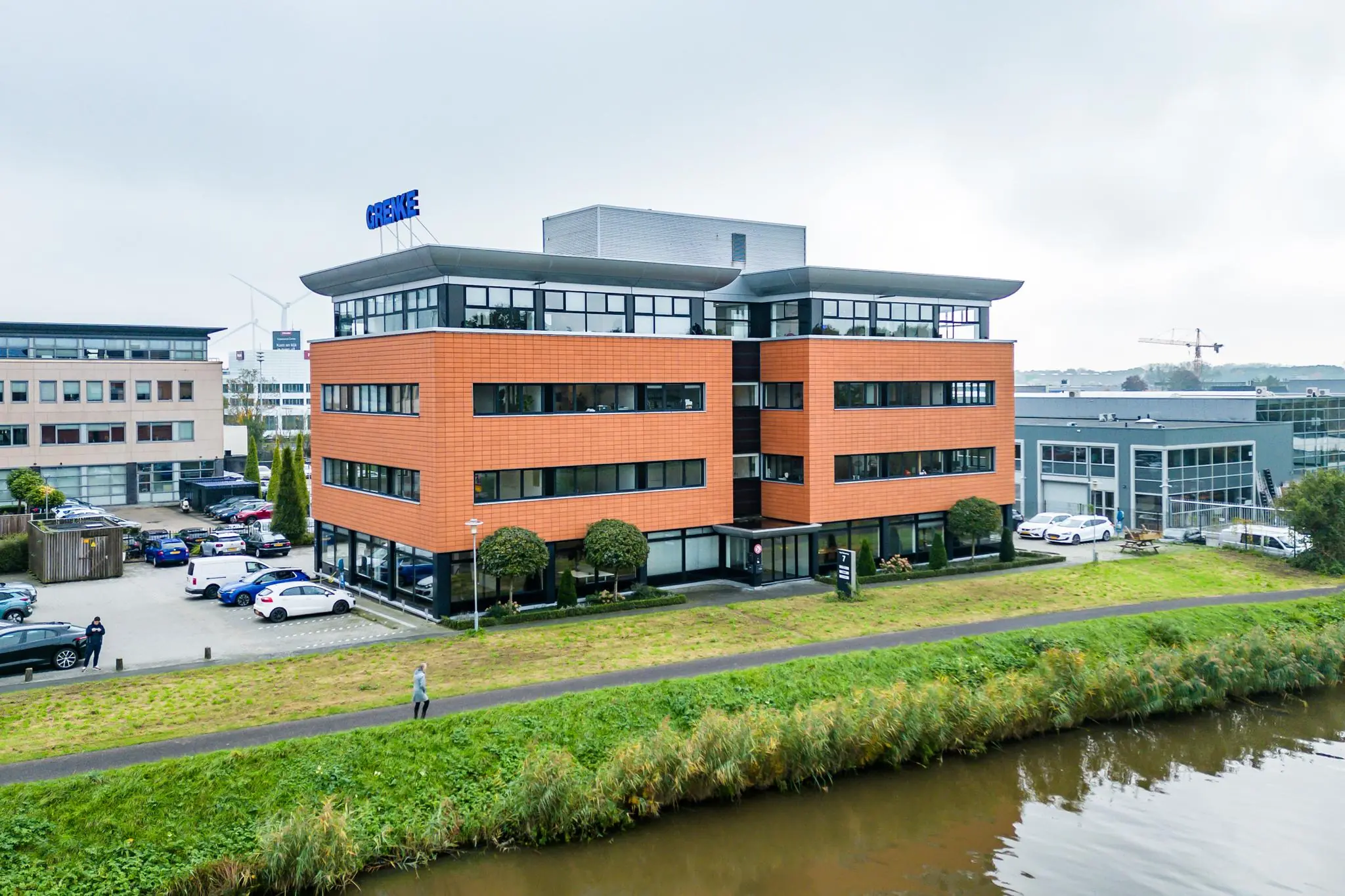 Kantoorgebouw van GRENKE aan de Lage Biezenweg met parkeerplaats en waterpartij op de voorgrond.